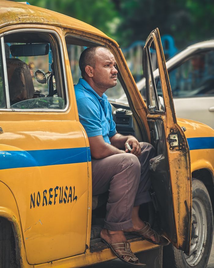 services-02 A man sits in an iconic yellow taxi in Kolkata, India, conveying local transportation essence.