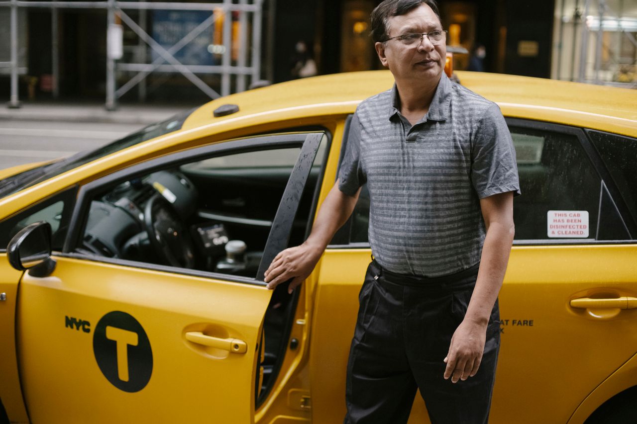 services-01 Serious crop ethnic male in casual clothes and eyeglasses standing near modern yellow taxi parked on street in New York and looking away
