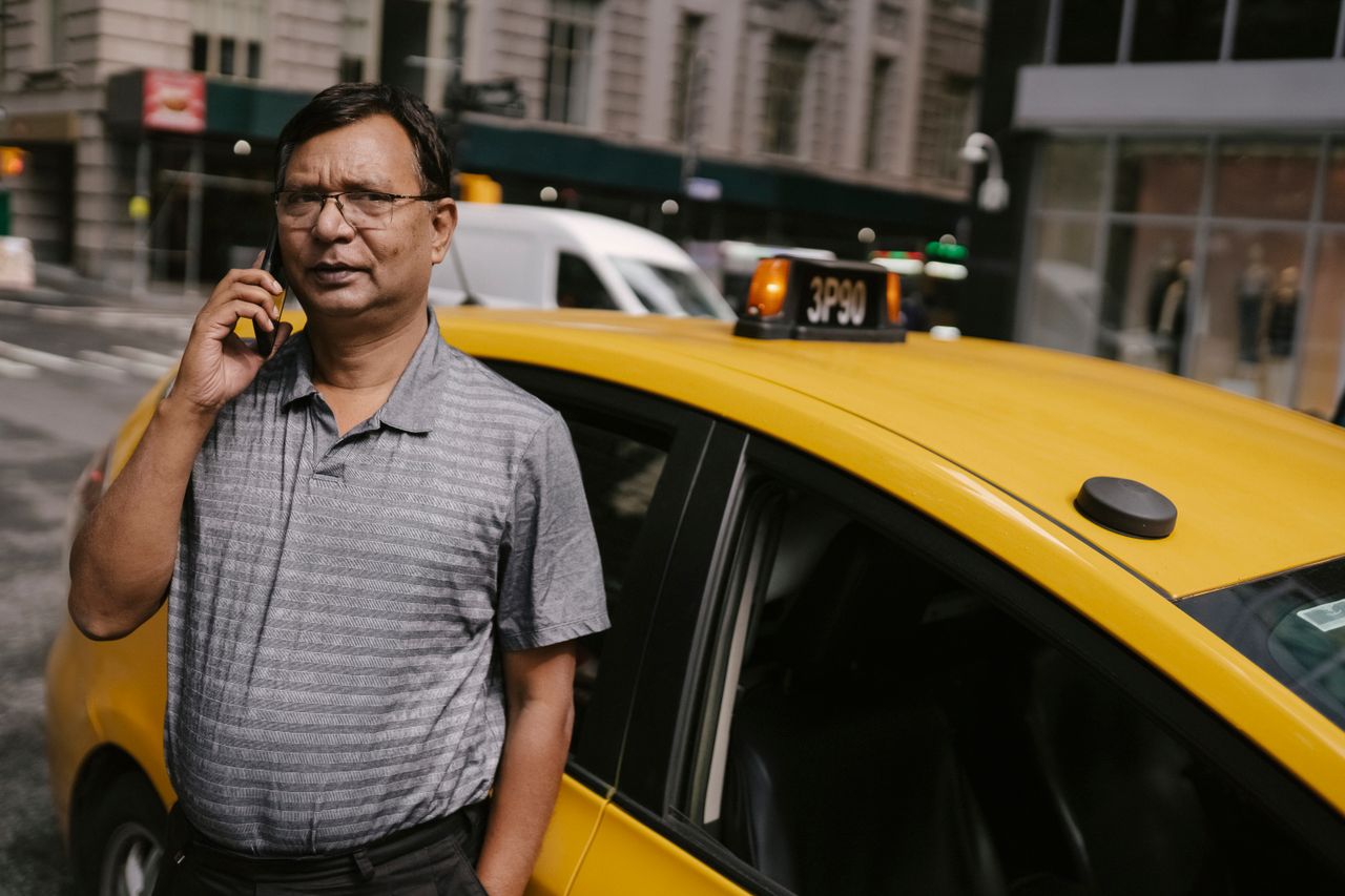 services-03 Serious ethnic male standing near yellow car while having conversation with client on phone